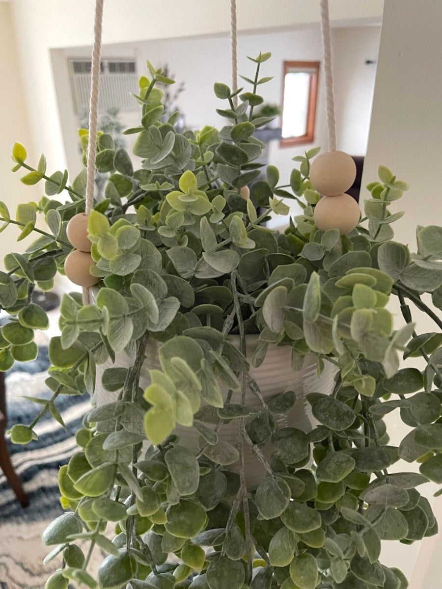 close up for realistic faux eucalyptus plant with overlapping stems in hanging white ceramic pot on white strings