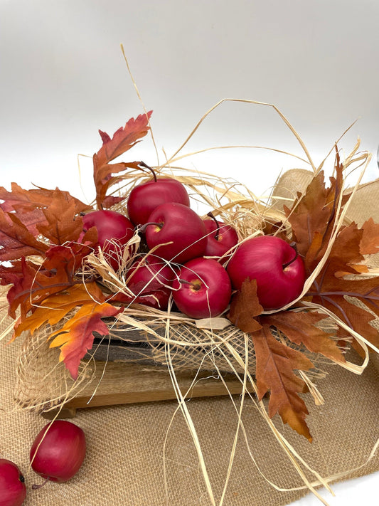 Decorative arrangement with red apples, brown leaves, and straw in wooden crate