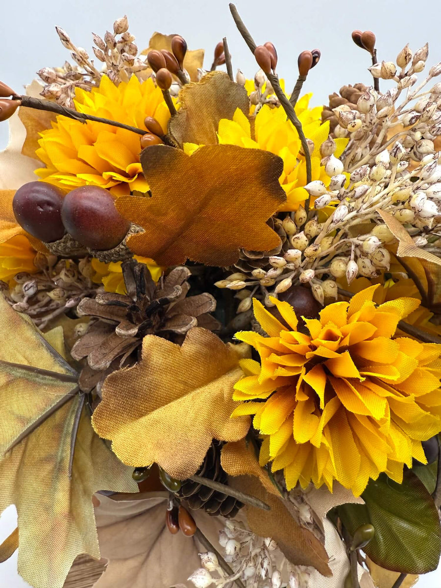 close up for autumn arrangement with flowers, leaves, pinecones, wheat stems in ywllow, beige, brown colors on dusty orange wooden pumpkin