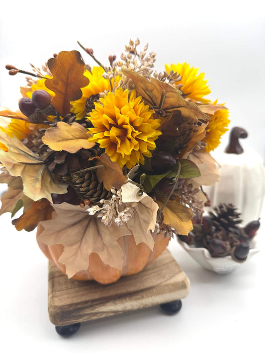 autumn arrangement with flowers, leaves, pinecones, wheat stems in ywllow, beige, brown colors on dusty orange wooden pumpkin