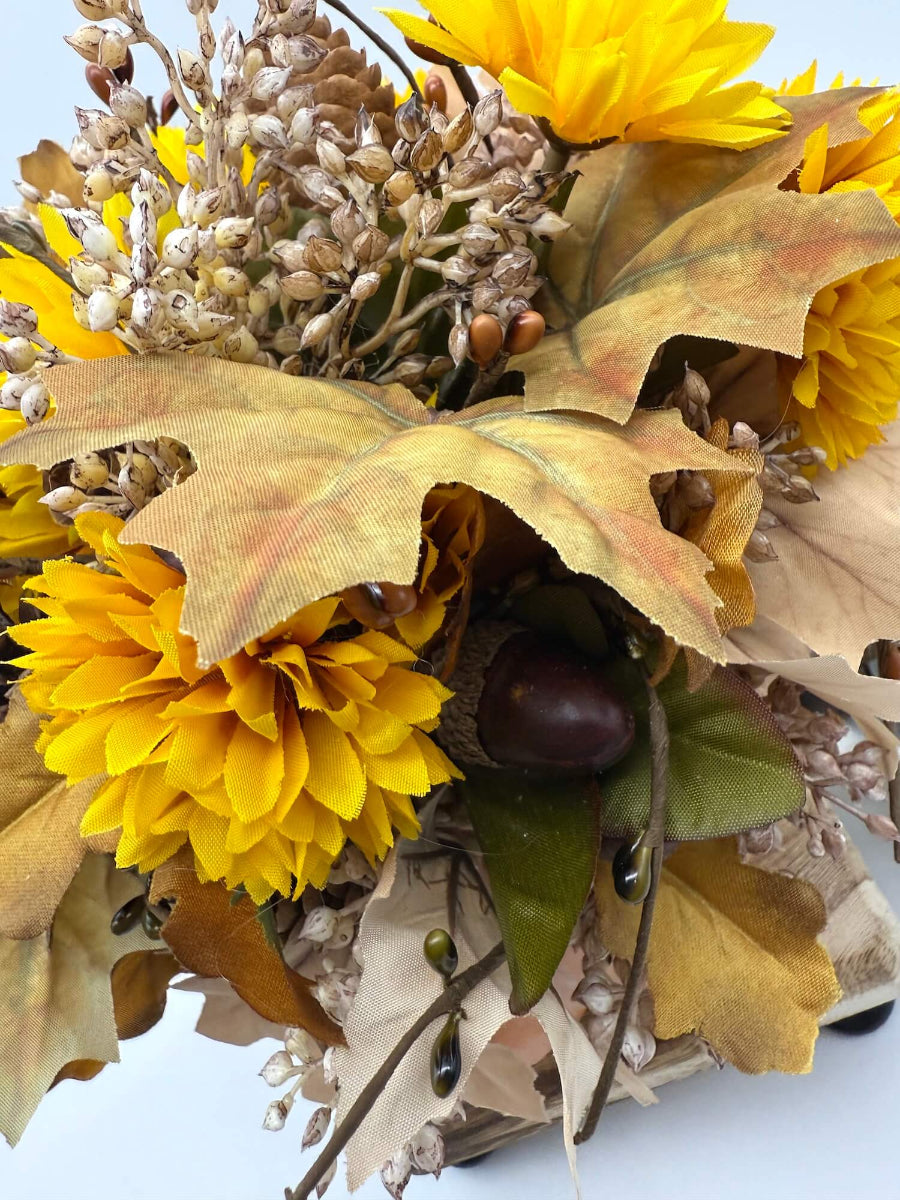 autumn arrangement with flowers, leaves, pinecones, wheat stems in ywllow, beige, brown colors on dusty orange wooden pumpkin