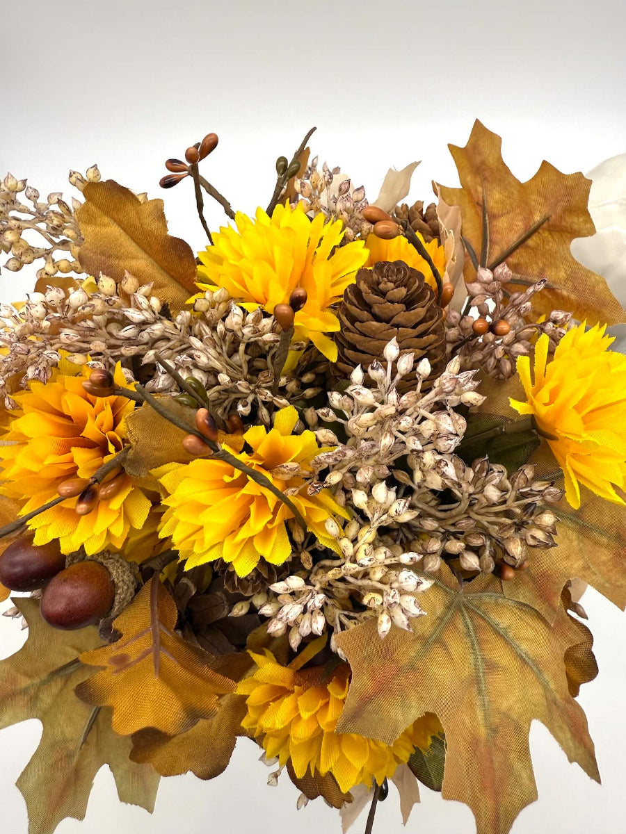 view from top for autumn arrangement with flowers, leaves, pinecones, wheat stems in ywllow, beige, brown colors on dusty orange wooden pumpkin