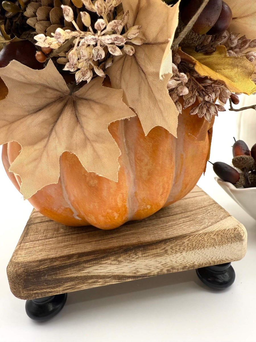 close up for autumn arrangement with flowers, leaves, pinecones, wheat stems in ywllow, beige, brown colors on dusty orange wooden pumpkin
