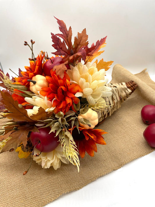 Cornucopia filled with autumn-themed flowers and leaves and autumn berries