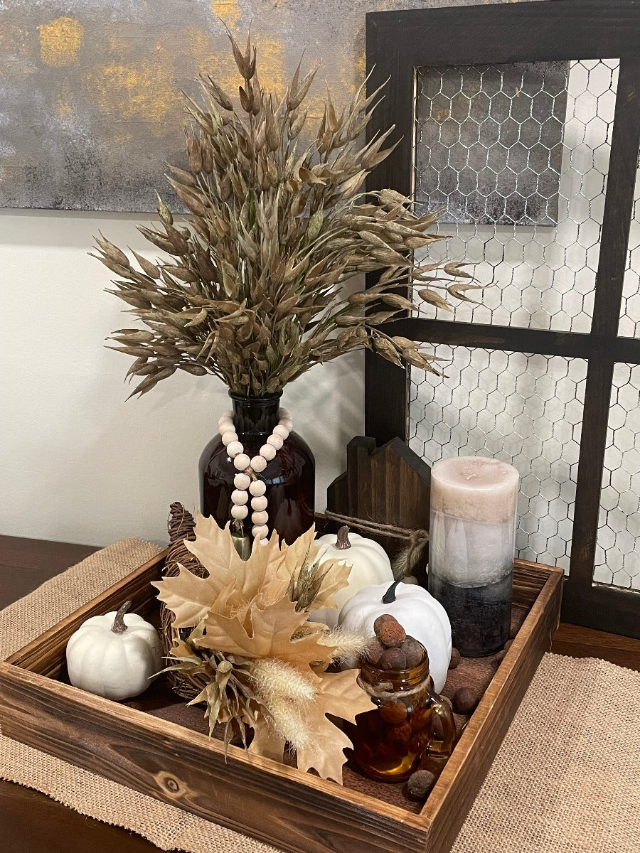 Fall Tray Decor with wheat arrangement in brown lass bottle vase, jar with faux acorns, white faux pumpkins, candle, wooden home sign on square wooden tray