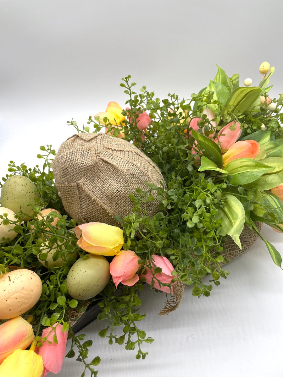 yellow pink orange fake tulips with artificial bright greenery and faux eggs of different sizes and shapes in wooden planter