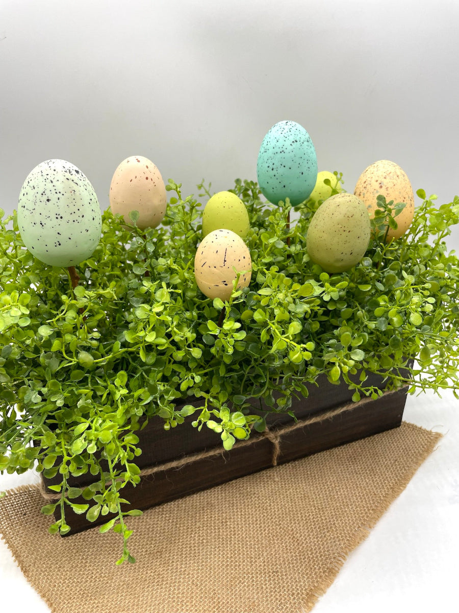 realistic greenery centerpiece with easter eggs in pastel colors in wooden planter in expresso color