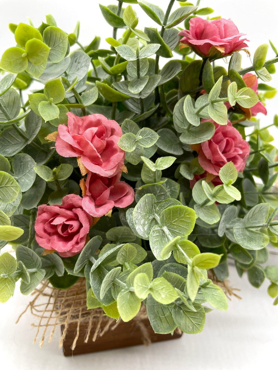 close up for faux eucalyptusarrangement with smoked pink roses in wooden planter decorated with burlap