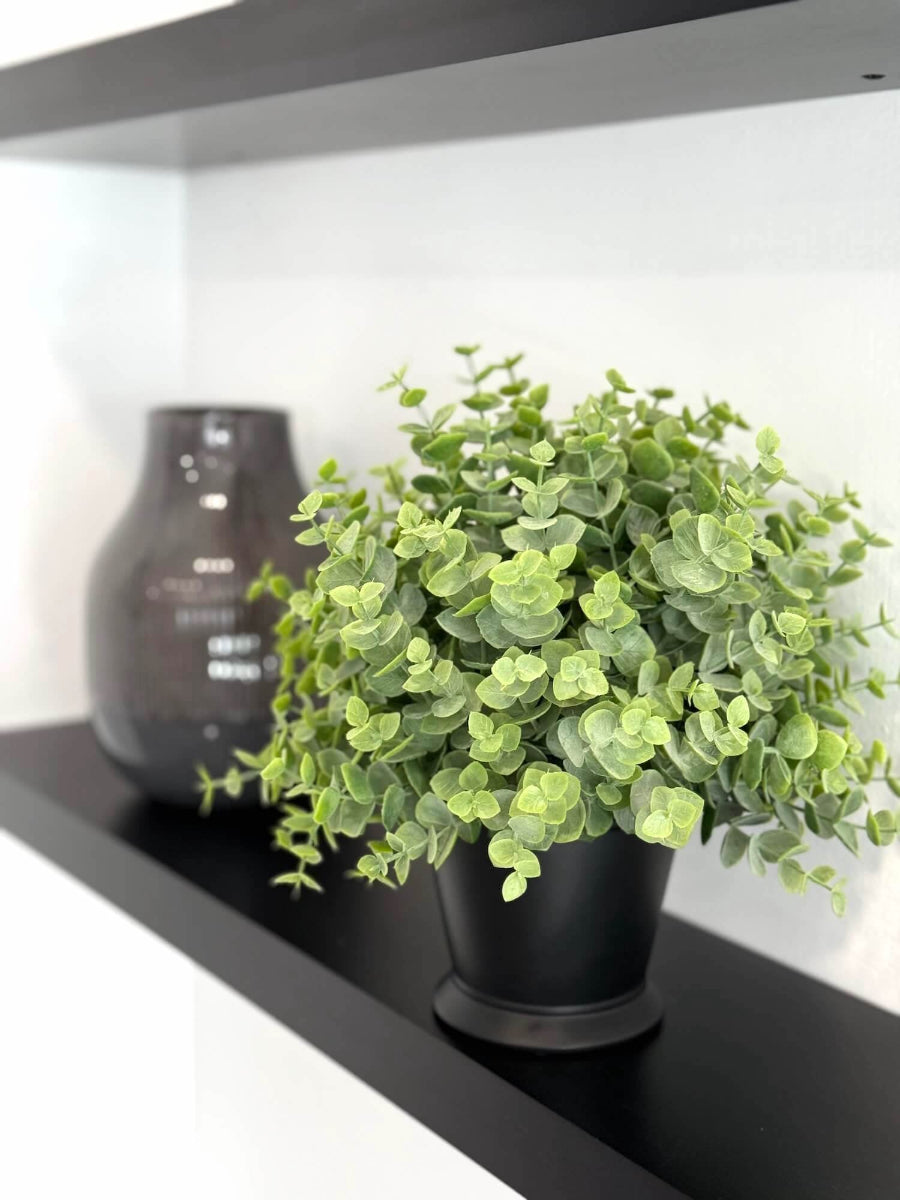 realistic looking faux eucalyptus arrangement in black ceramic vase on a shelf