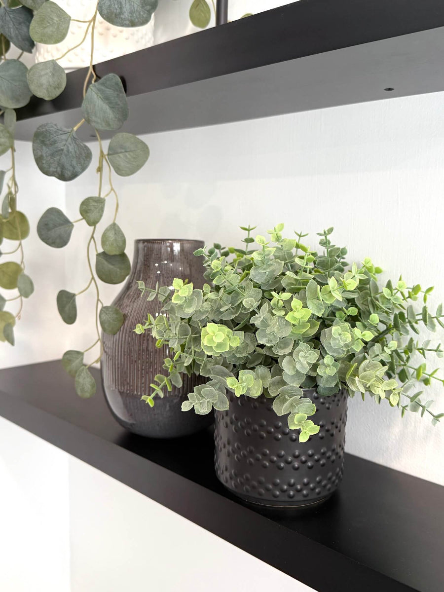 realistic faux eucalyptus plant in textured black ceramic vase