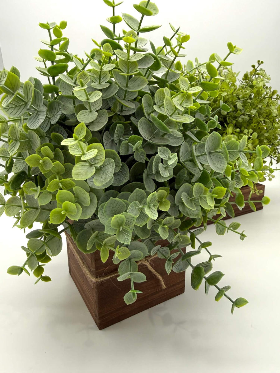 close up for faux eucalyptus arrangement in wooden planter square vase decorated with jute