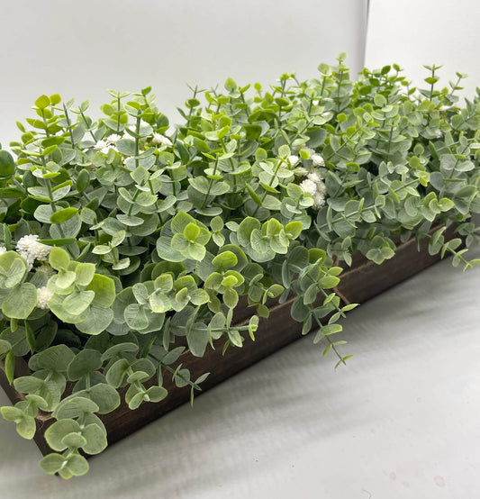 realistic looking faux eucalyptus arrangement with delicate white flowers in long wooden planter stained in espresso color and decorated with jute