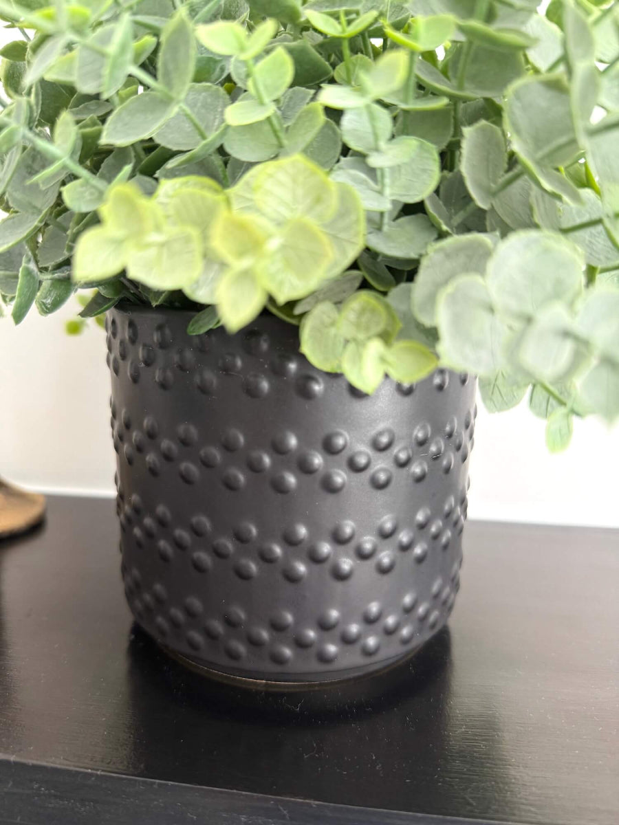 close up for realistic looking green faux eucalyptus plant in elegant textured black matte ceramic pot 