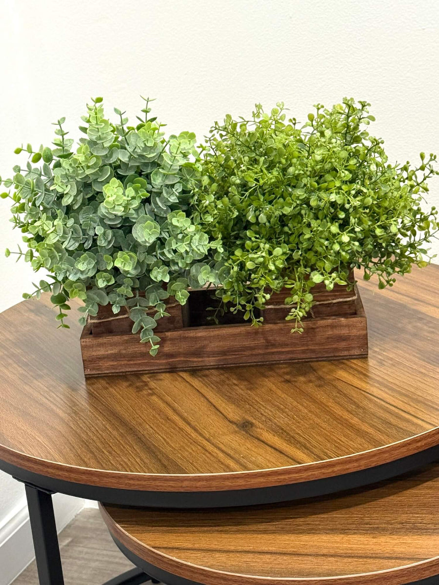 Two potted plants in a wooden planter on a wooden table - faux eucalyptus and vivid greenery