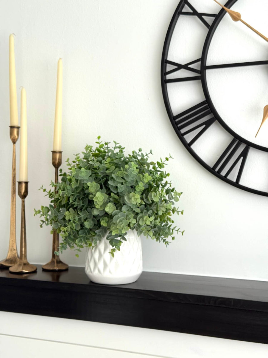 realistic faux eucalyptus plant in white ceramic pot vase of diamond pattern on mantel shelf