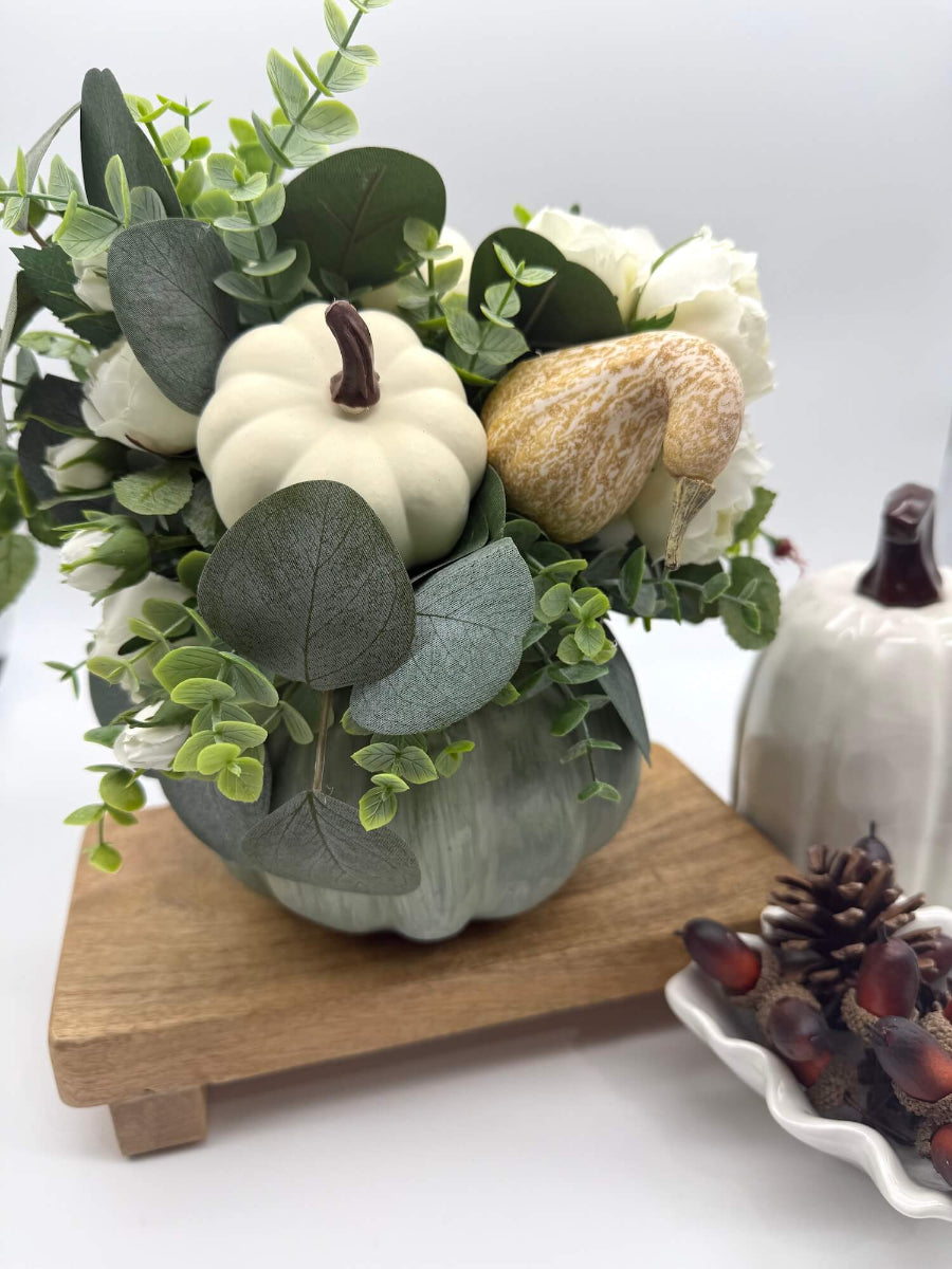 fall centerpiece with white roses, eucalyptus stem, ivory and beige pumpkins on wooden pumpkin in sage color