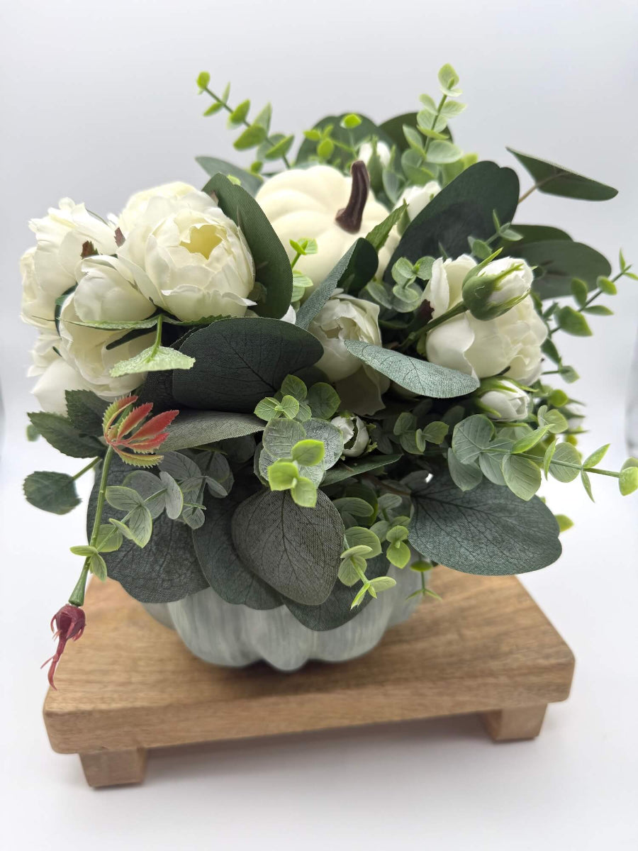back side of fall centerpiece with white roses, eucalyptus stem, ivory and beige pumpkins on wooden pumpkin in sage color