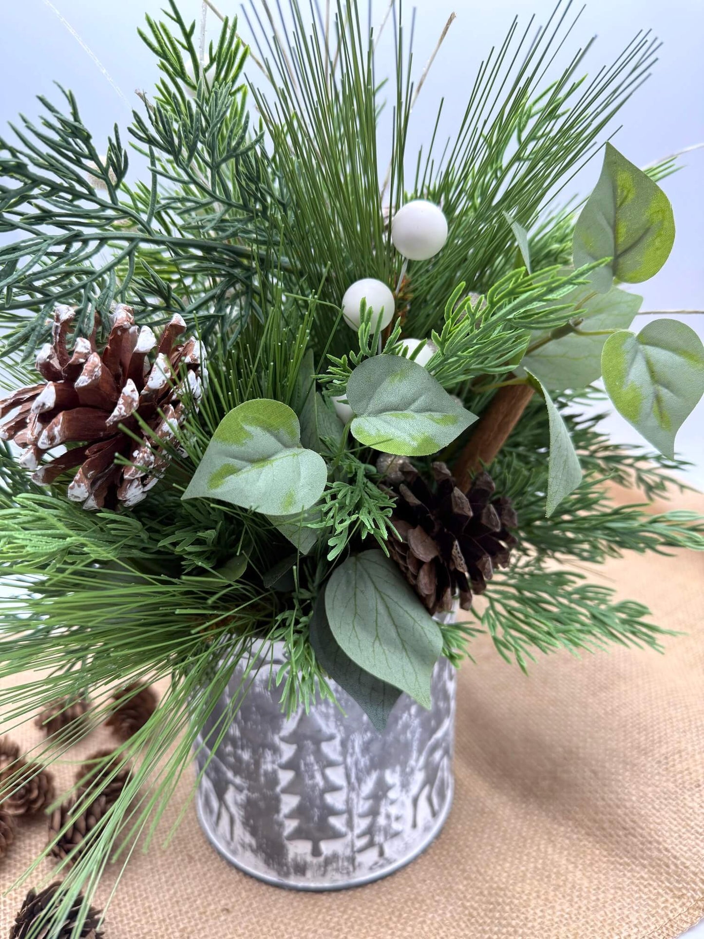 back of Decorative arrangement of greenery and pinecones in a small metal tin with forest design