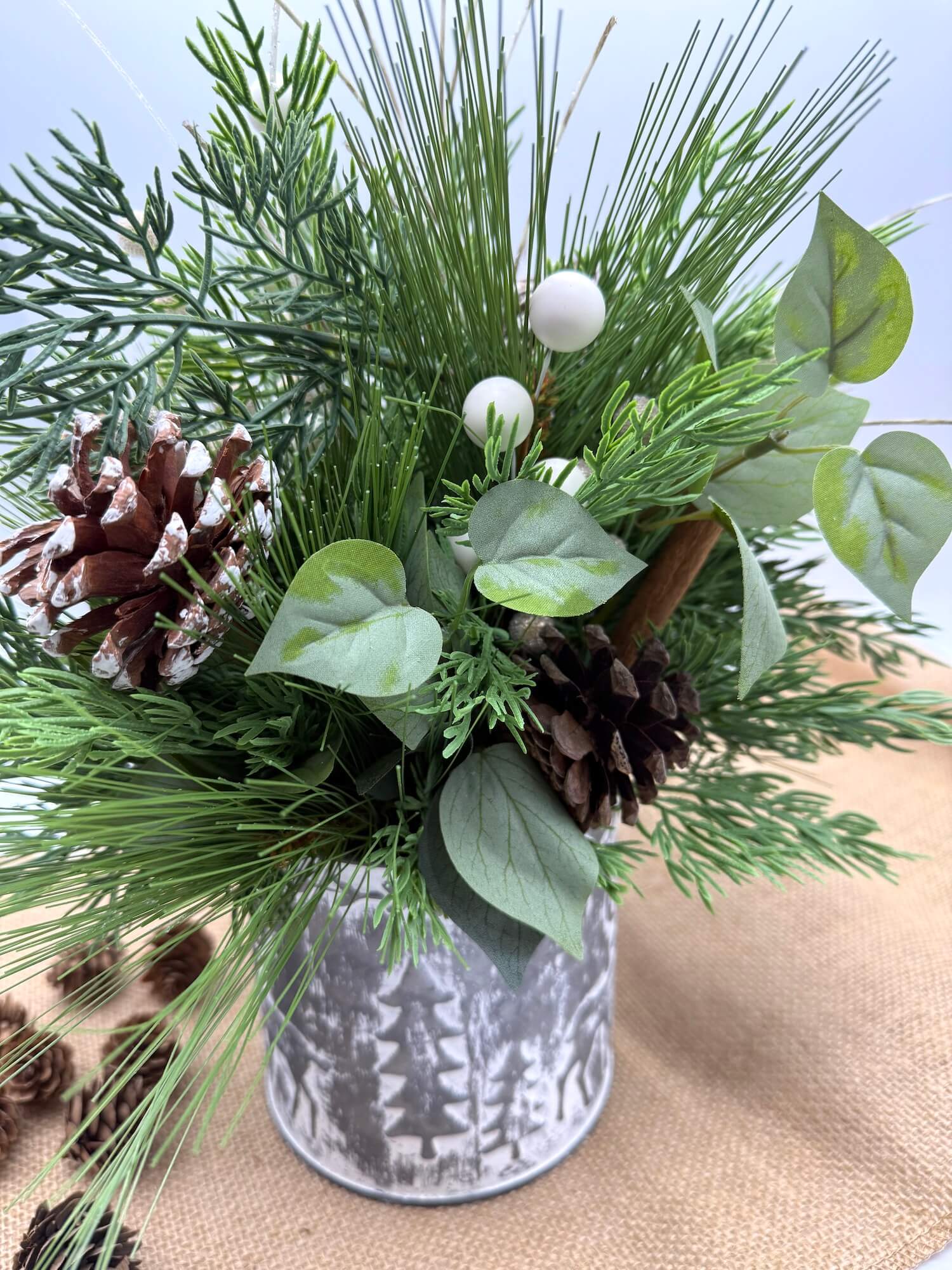 back of Decorative arrangement of greenery and pinecones in a small metal tin with forest design