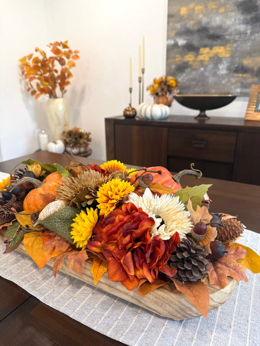 rich harvest thanksgiving centerpiece in long wooden vessel with faux flowrs, pumpkin, fall leaves and berries in brown, yellow, orange