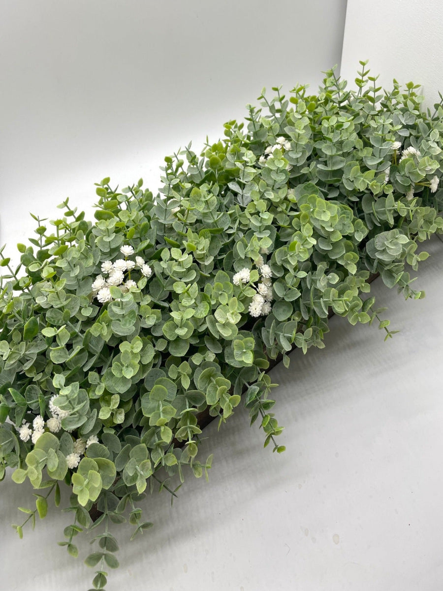 view from top on lush and realistic green eucalyptus centerpiece with white delicate flowers set in wooden planter 
