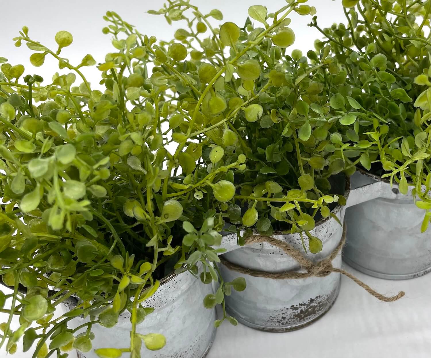 close up of vivid green faux greenery in triple can metal galvanized planter with handles decorated with jute, in modern farmhouse style