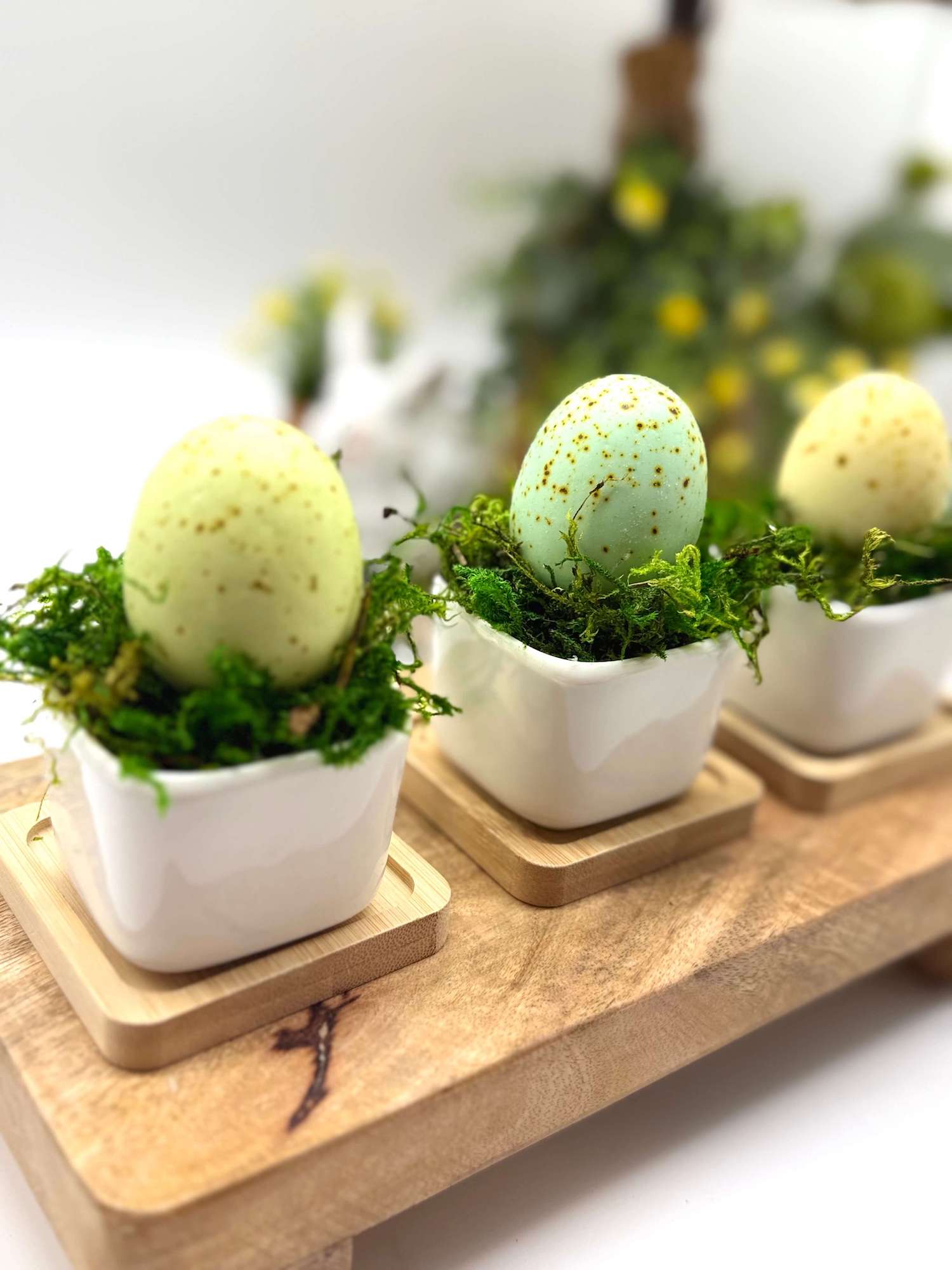 mini faux eggs in pastel colors placed in white shiny ceramic vase finished with green moss