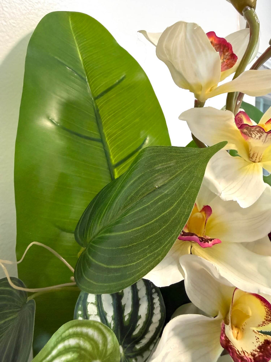 close up for realistic looking tall faux white orchid arrangement accompanied with greenery in black matte textured ceramic vase