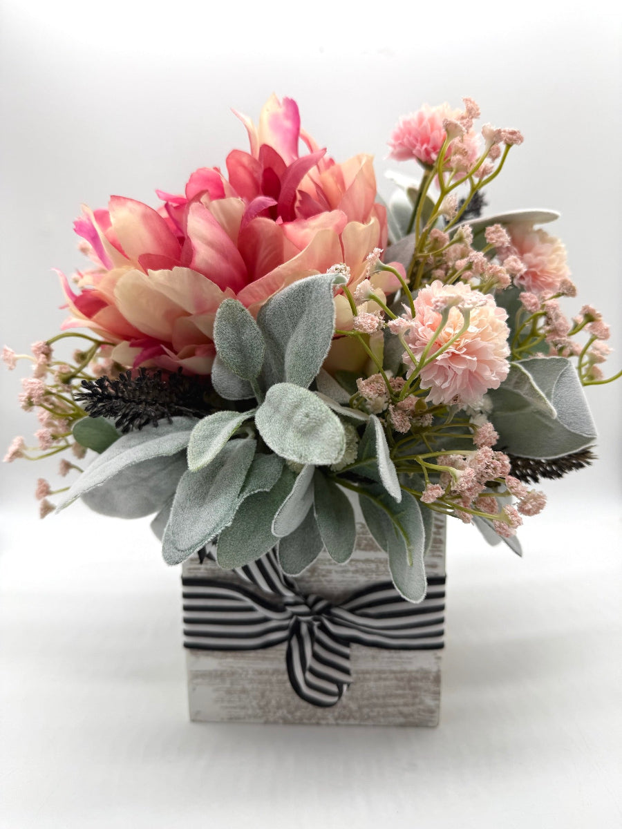 handmade floral arrangement with pink peony and other pink/white flowers and lambs ear greenery in white wooden vase with black white ribbon