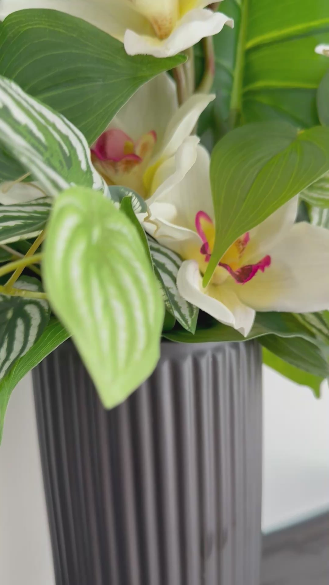 video of realistic looking elegant white orchid arrangement with greenery and decorative foliage in black textured ceramic vase