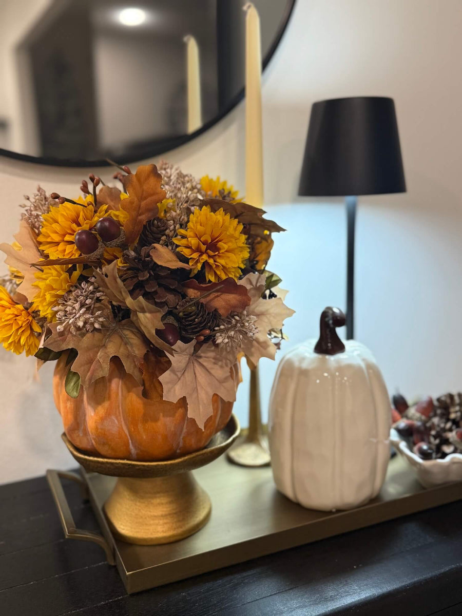pumpkin arrangement with fall flowers, leaves, wheat stems created on orange wooden pumpkin styled on console table