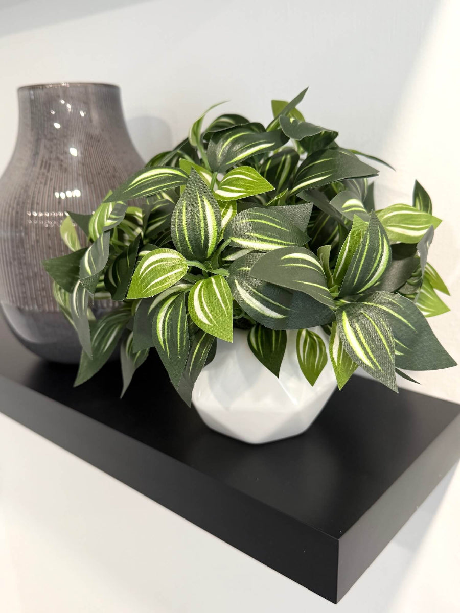 realistic looking faux plant with green leaves and white stripes in white geometric ceramic pot vase styled on a shelf