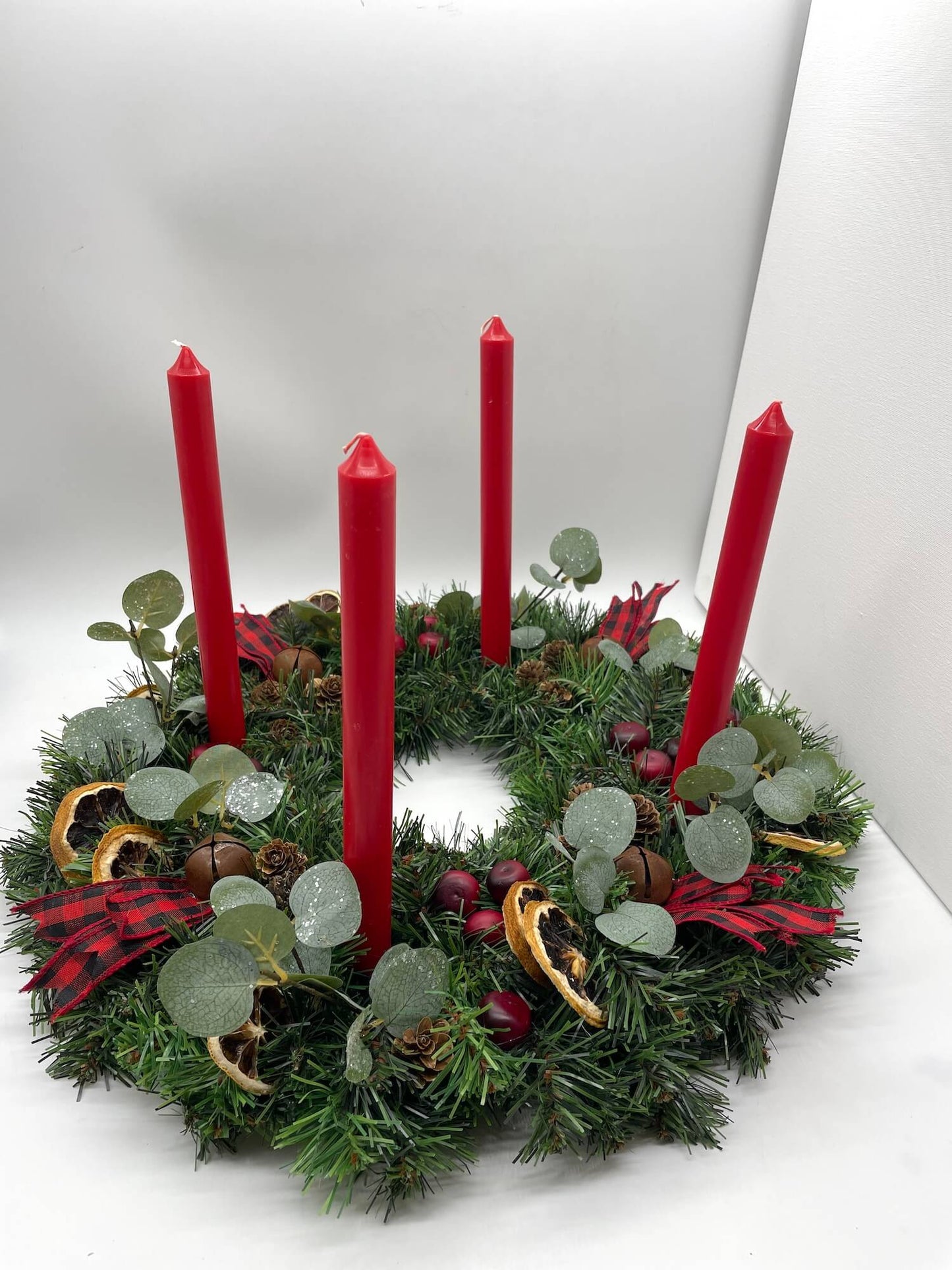 christmas advent wreath with natural elements of cranberries, dried lemon slices, pinecones, metal bells and red-black ribbon for rustic look with red  tapper candles
