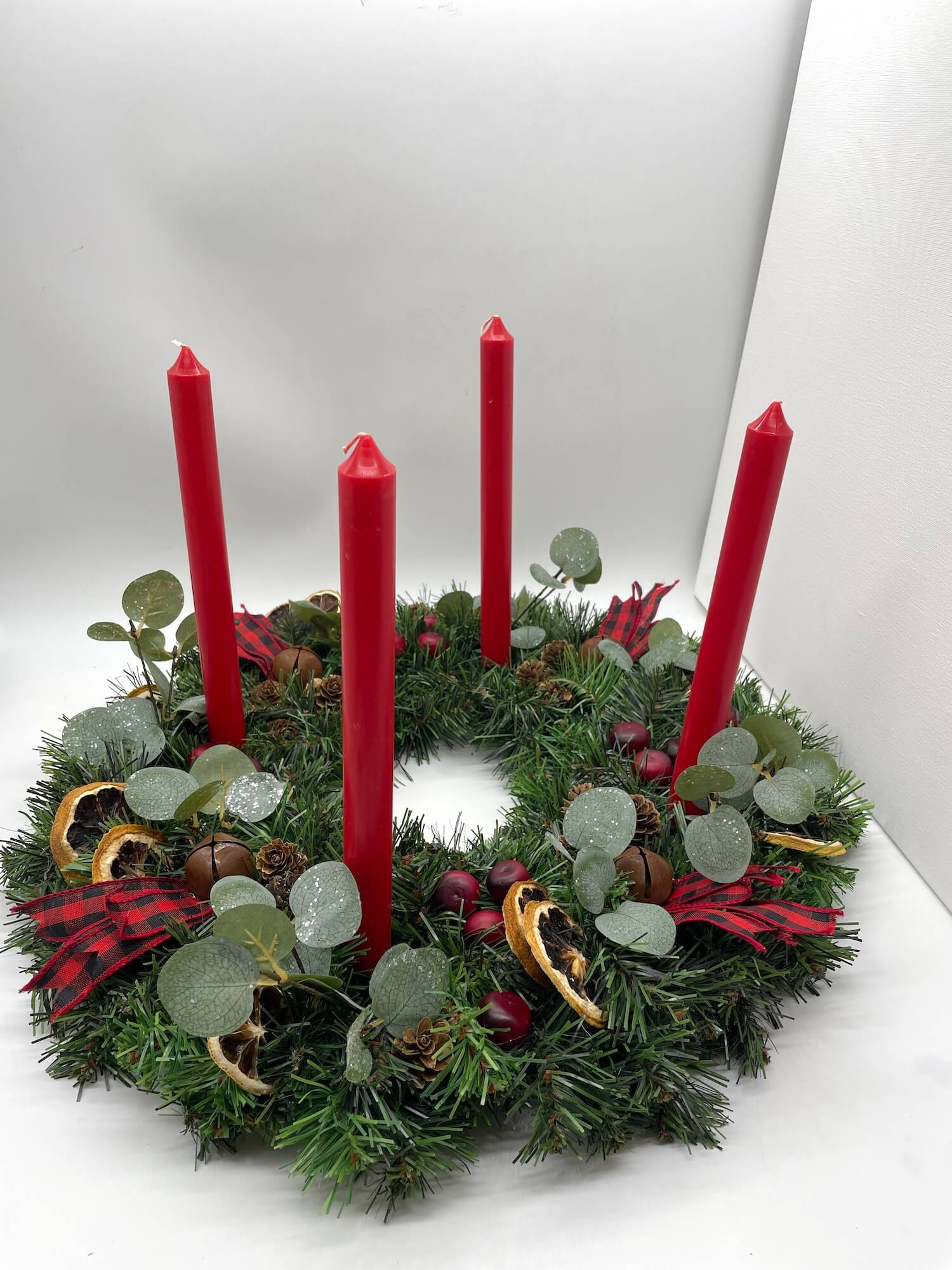 christmas advent wreath with natural elements of cranberries, dried lemon slices, pinecones, metal bells and red-black ribbon for rustic look with red  tapper candles