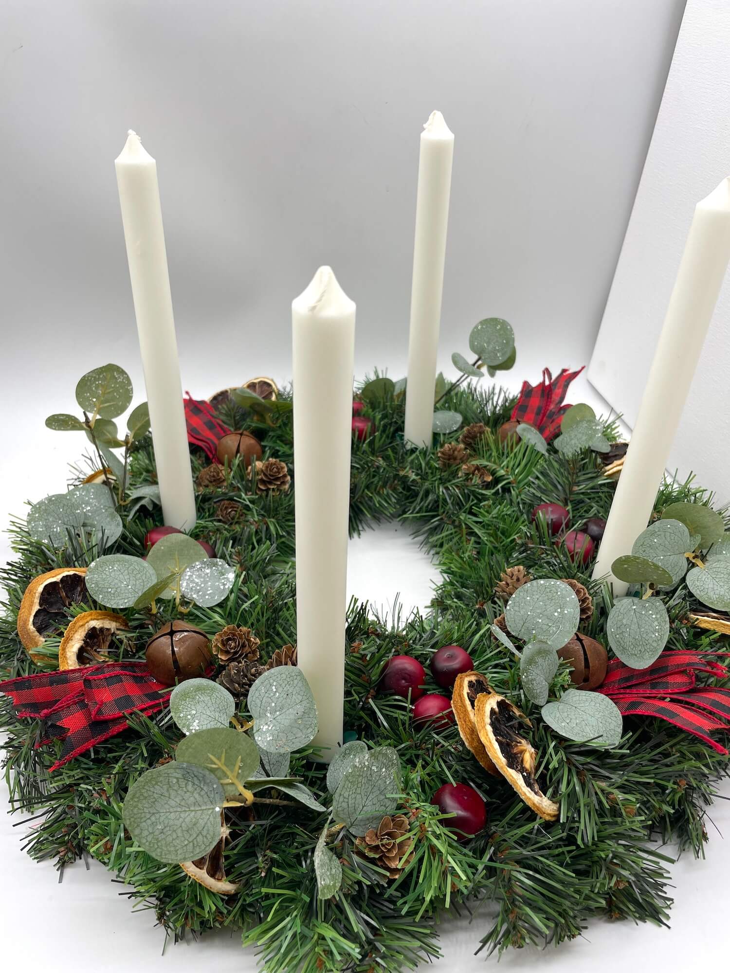advent wreath with natural elements of cranberries, dried lemon slices, pinecones, metal bells and red-black ribbon for rustic look with white tapper candles