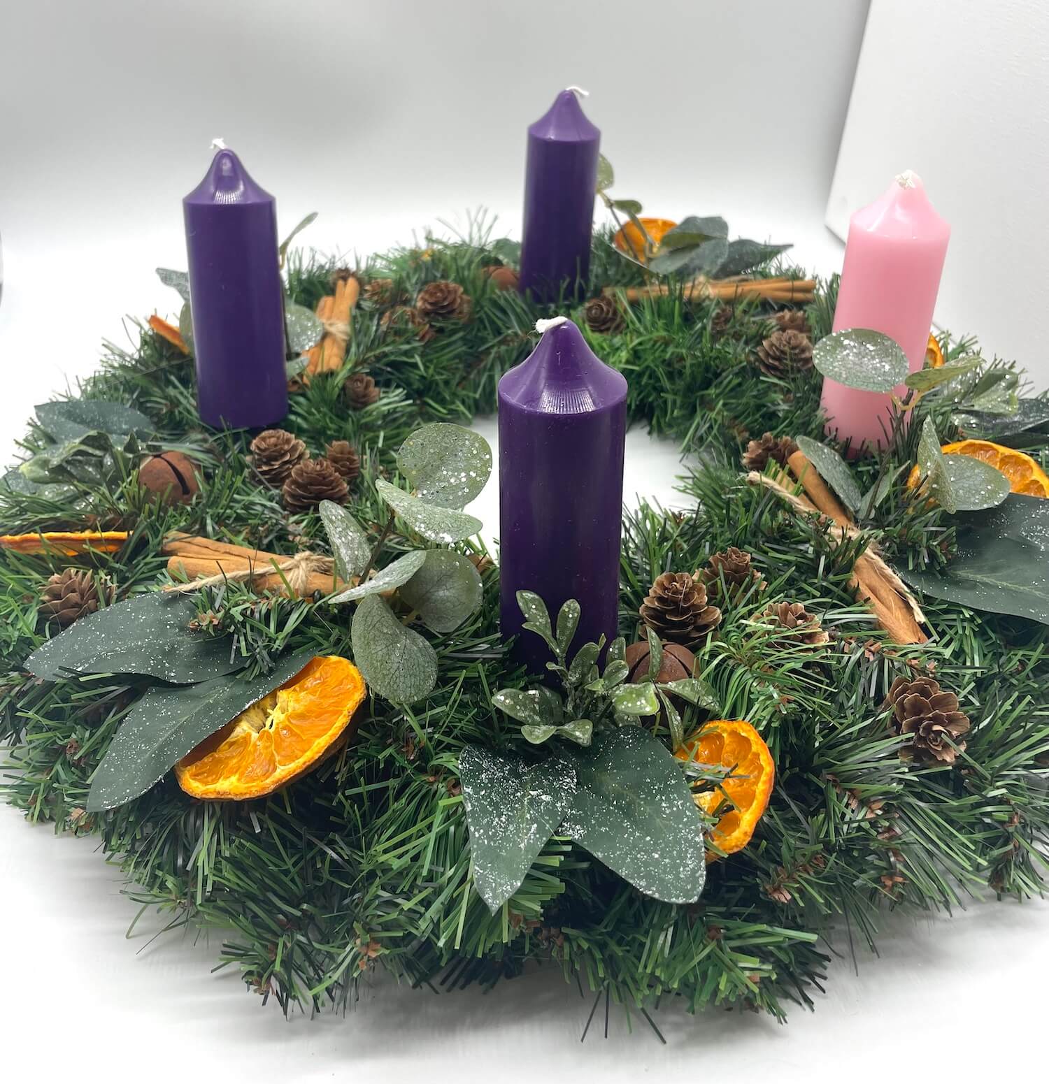 rustic Advent wreath with pink purple candles and earthy elements of orange dried slices, cinnamon sticks, pinecones, brown metal bells and winter greenery