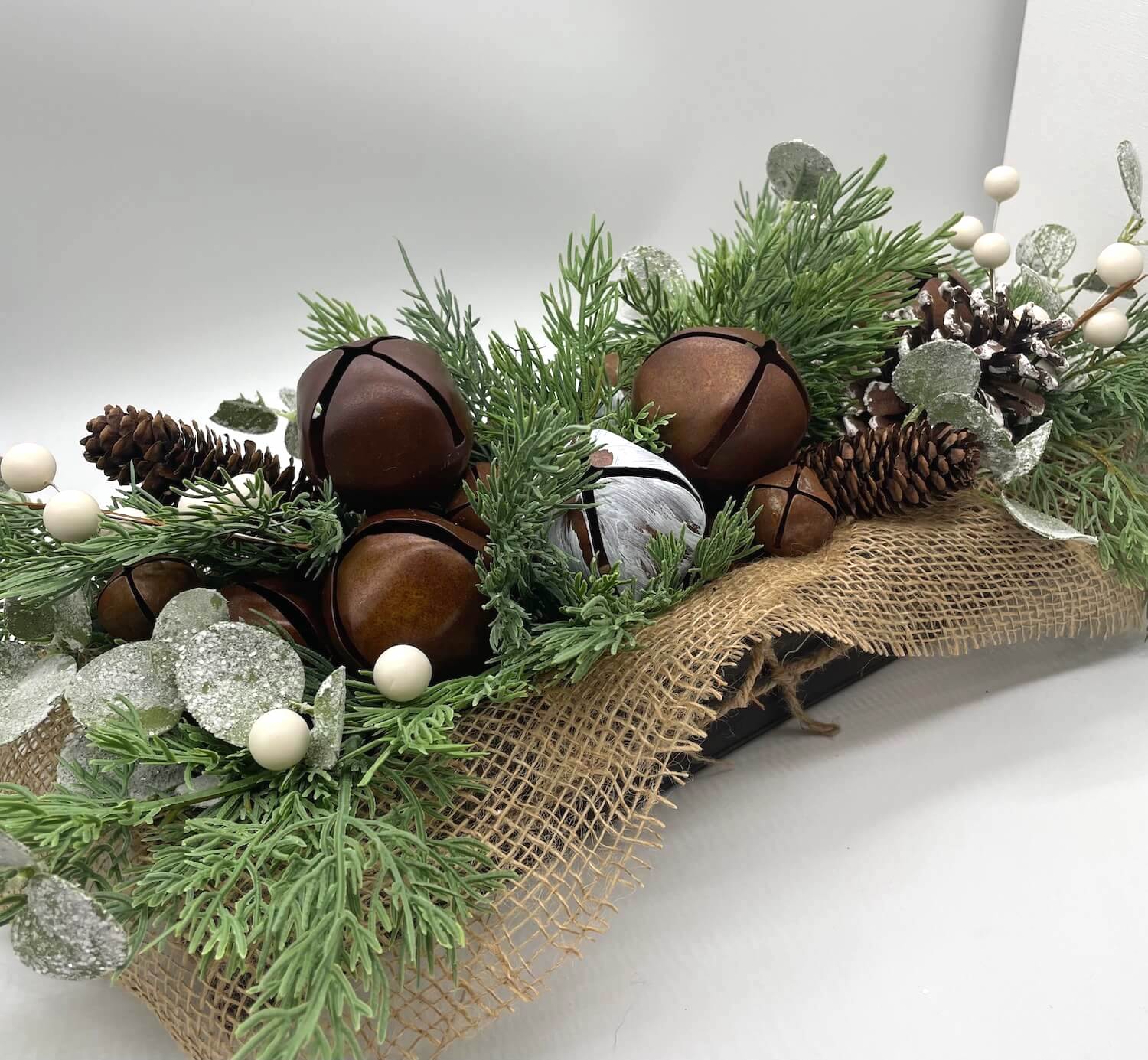 Decorative arrangement with greenery, pinecones, metal bells finished with burlap