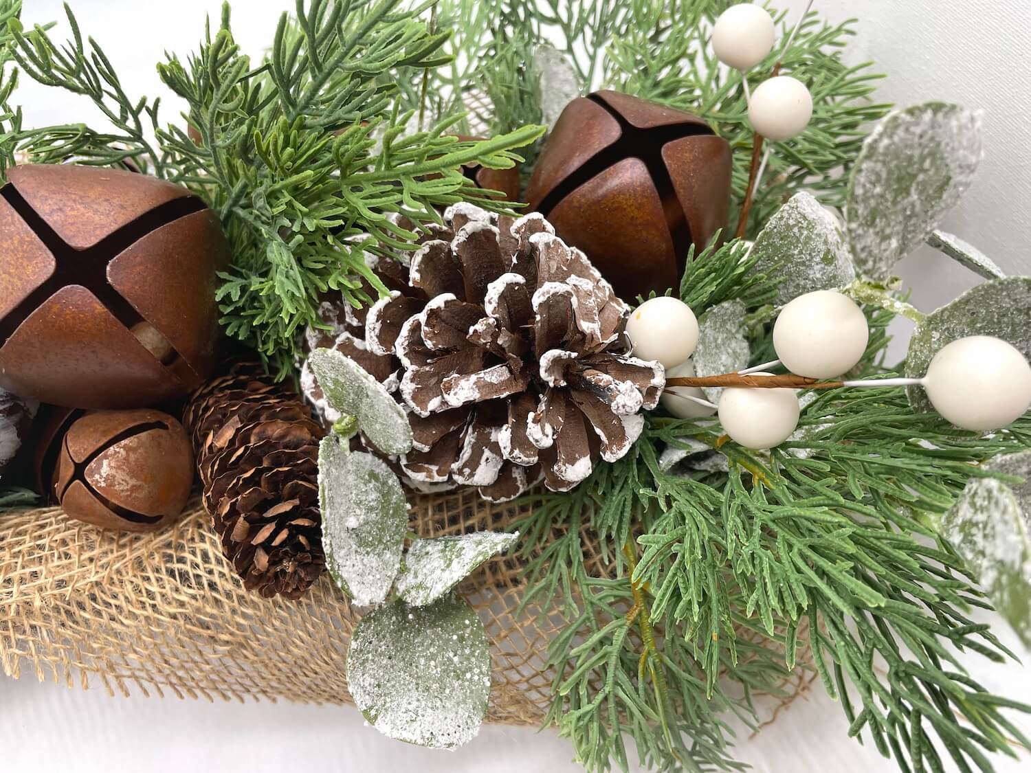 close up of winter centerpiece with pinecones, metal bells, variety of greenery