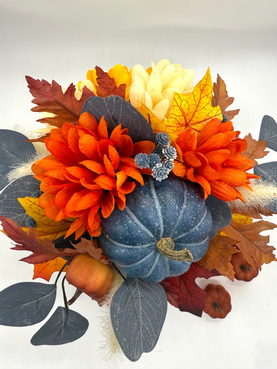 Autumn-themed floral arrangement in blue and orange with pumpkins, flowers and leaves in black vase