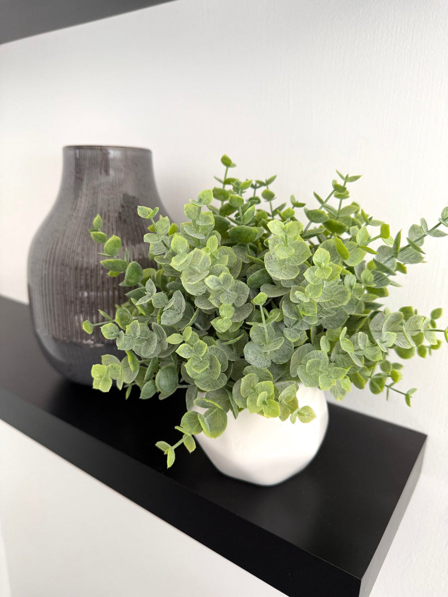 realistic looking faux eucalyptus arrangemnt in white ceramic pot vase of geometric shape