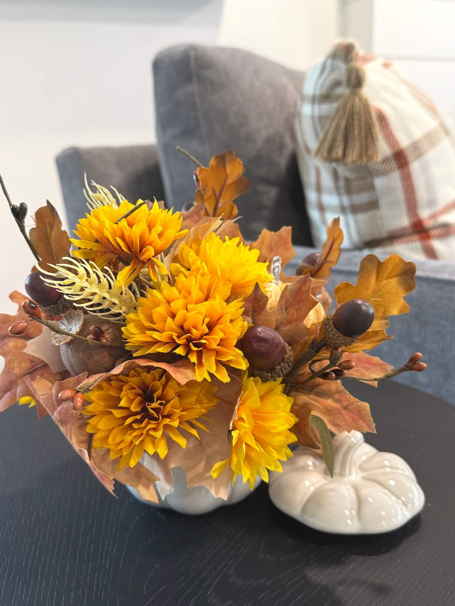 lush elegant handmade small fall arrangement with yellow and gold flowers, brown leaves, poppy heads, acorns, pinecones in white ceramic pumpkin shaped vase