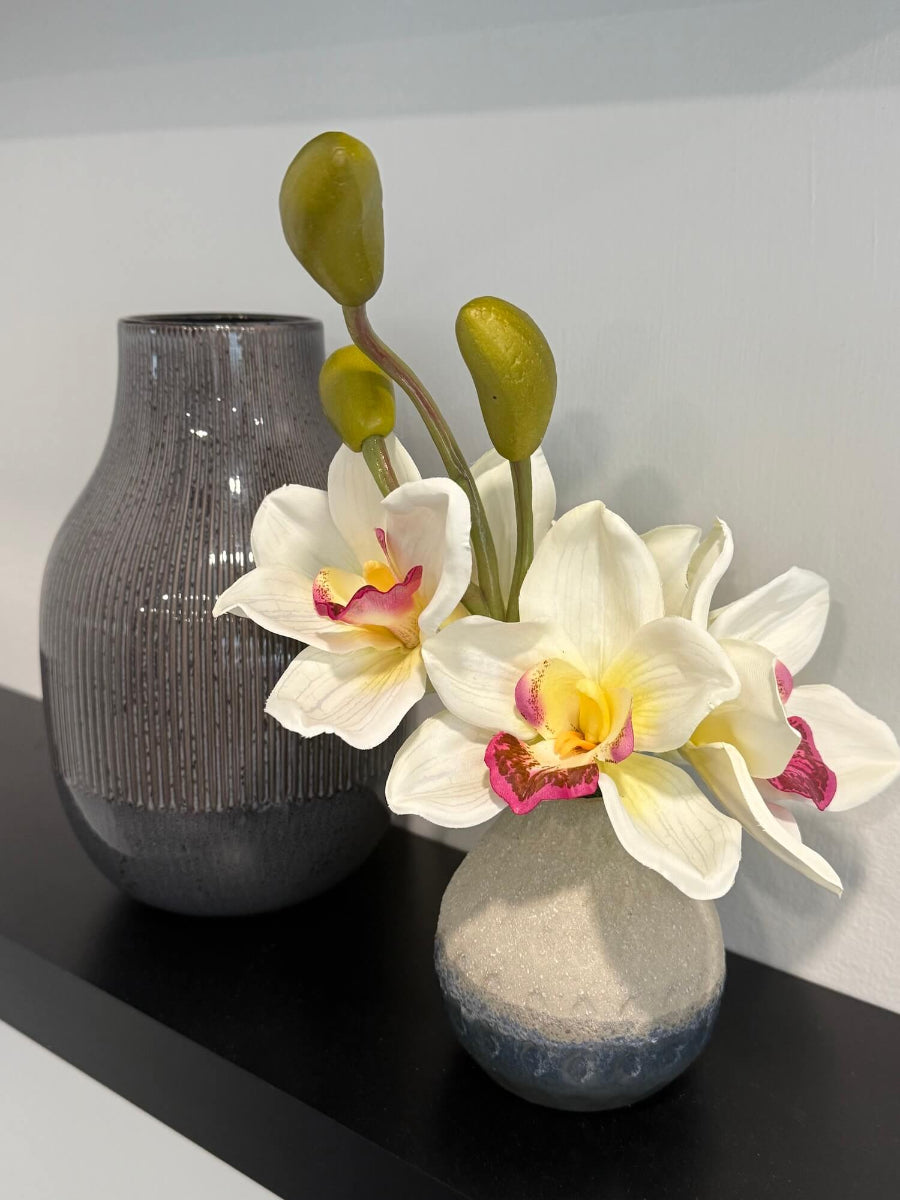 realistic looking small white orchid arrangement of five flowers and 3 buds in gray ceramic vase styled on shelf