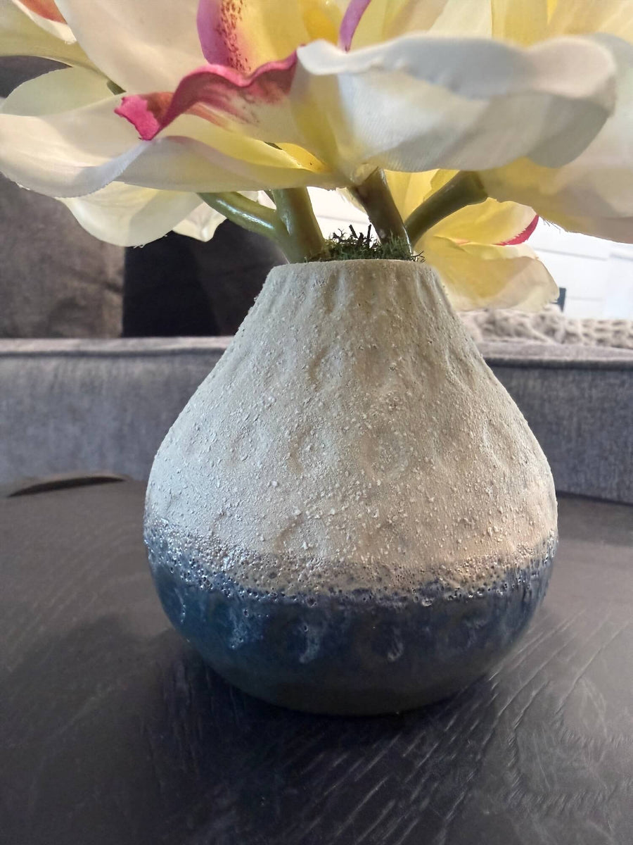 close up for vase of realistic looking small white orchid arrangement of five flowers and 3 buds in gray ceramic vase styled on coffee table