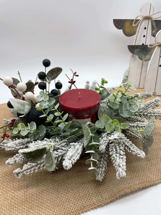 small table wreath with frosted evergreen and eucalyptus stems, red, white and black ornaments and red pillar candle in the middle