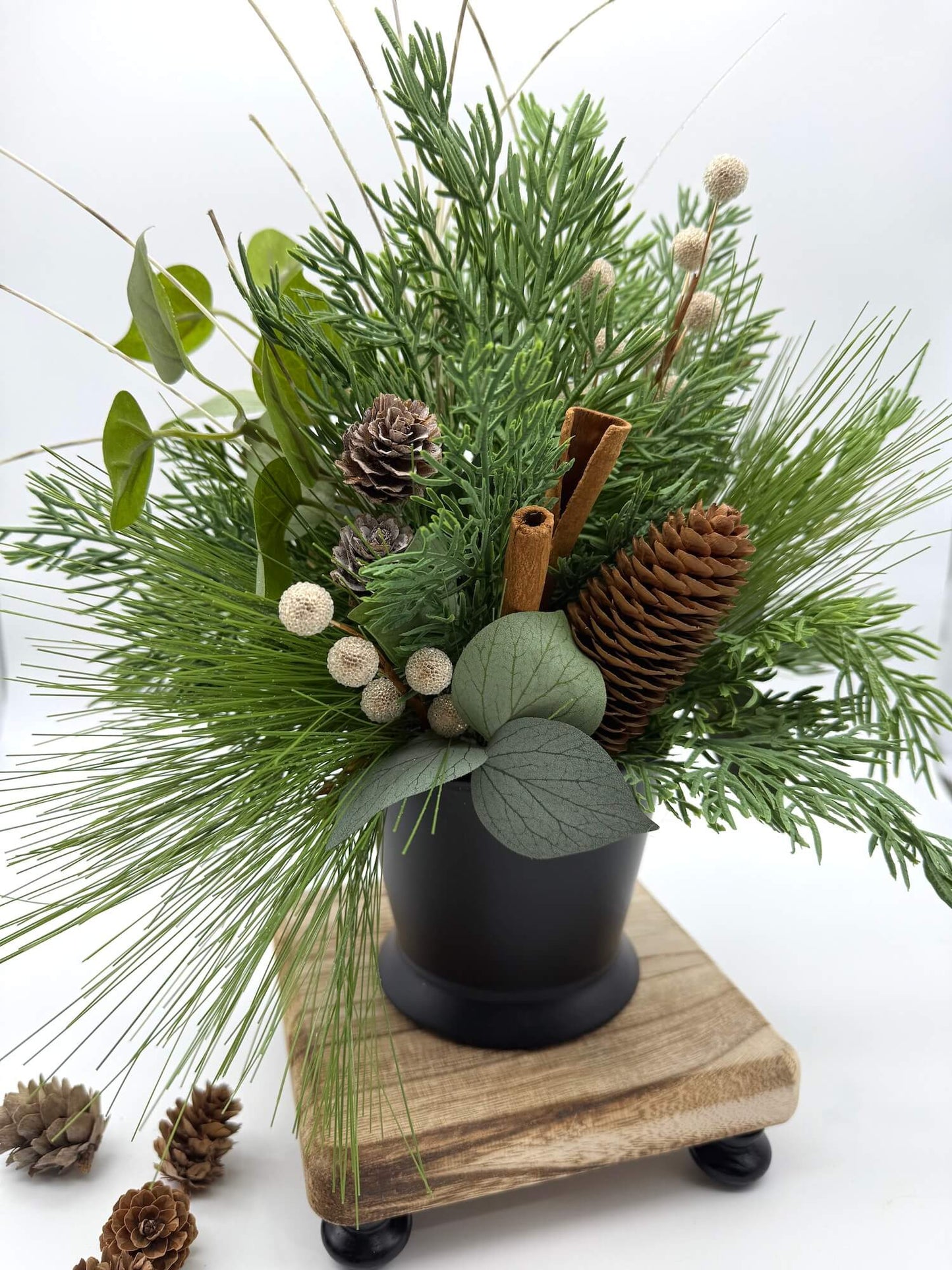 realistic looking variety of evergreen stems in black ceramic vase with cinnamon sticks, pinecones and berries