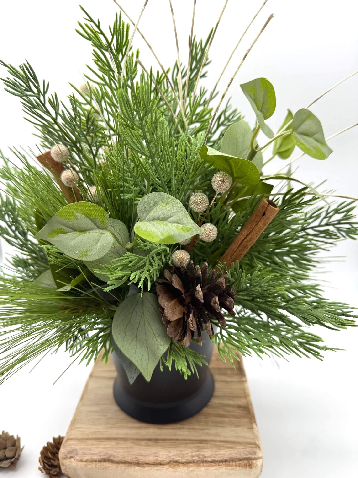 back of winter arrangement with greenery and evergreen in black ceramic vase with pinecones and cinnamon sticks