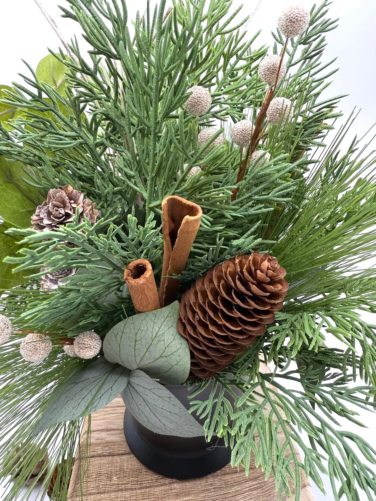 close up for evergreen stems in winter arrangements with pinecones and cinnamon sticks in neutral tones