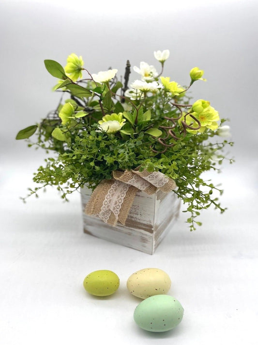 Spring centerpiece with green and white flowers, variety of greenery in whitewashed wooden vase decorated with burlap lace robbon