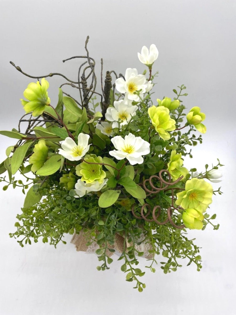 Spring arrangement with green and white flowers, variety of greenery in witewashed wooden vase decorated with burlap ribbon