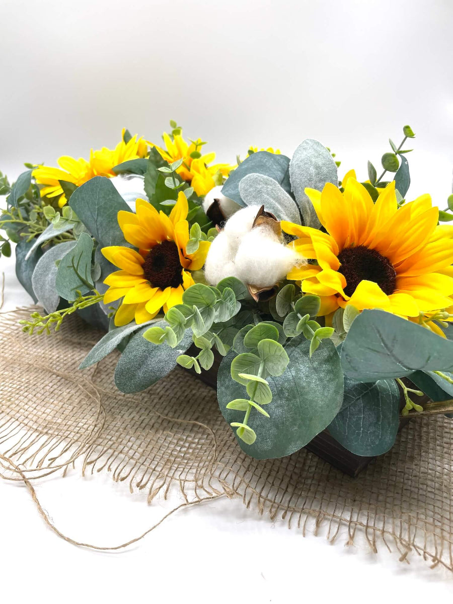 close up for yellow sunflower centerpiece with eucalyptus leaves and cotton stems in long wooden planter stained in expresso color